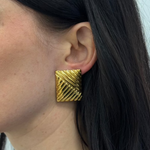 Eine Frau trägt elegante, goldene Ohrstecker in rechteckigem Design am Ohr.