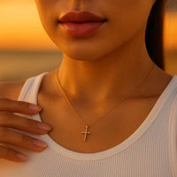 ahaufnahme einer Frau im weißen Top mit eleganter goldener Halskette und funkelndem Kreuzanhänger aus Zirkonia, aufgenommen im warmen Licht des Sonnenuntergangs