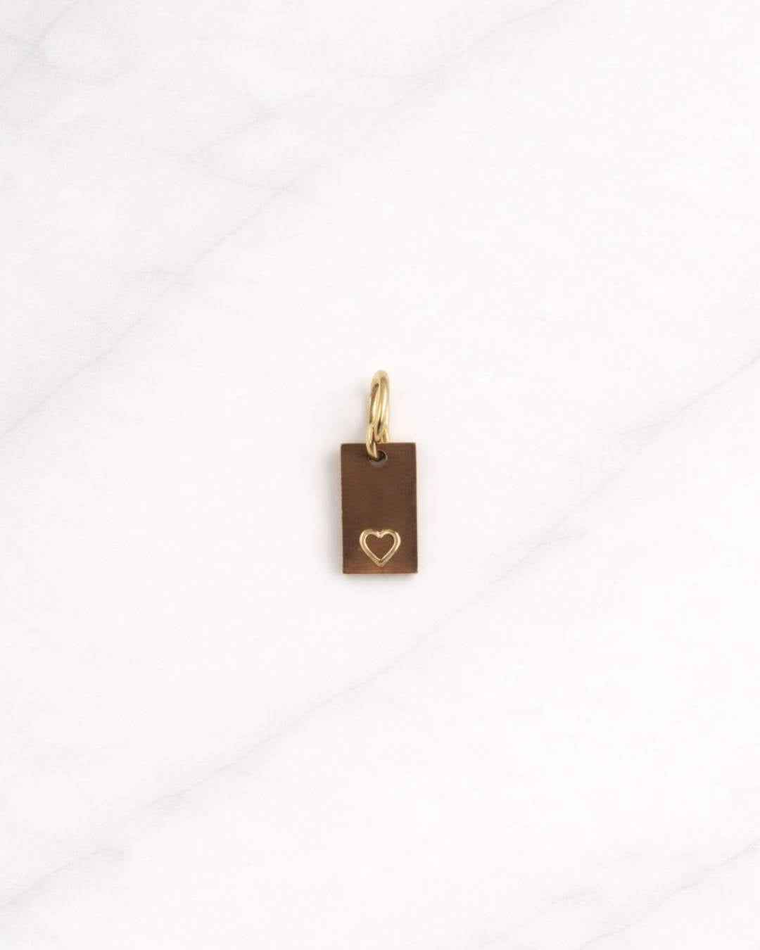 Aurelia CHARM goldfarbener rechteckiger Anhänger mit Herzdetail auf hellem Marmorphintergrund.