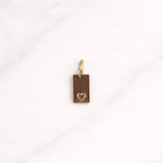 Aurelia CHARM goldfarbener rechteckiger Anhänger mit Herzdetail auf hellem Marmorphintergrund.
