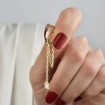 Detailaufnahme: goldene Hängecreole mit Zirkonia und Baguette-Anhänger wird in der Hand gehalten.