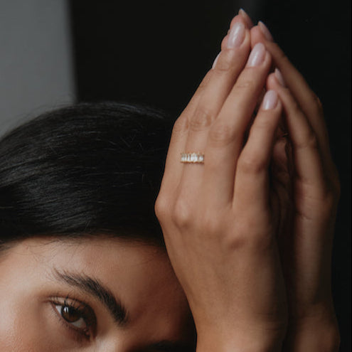 Goldener Baguette Ring an den gefalteten Händen einer Frau vor dunklem Hintergrund.
