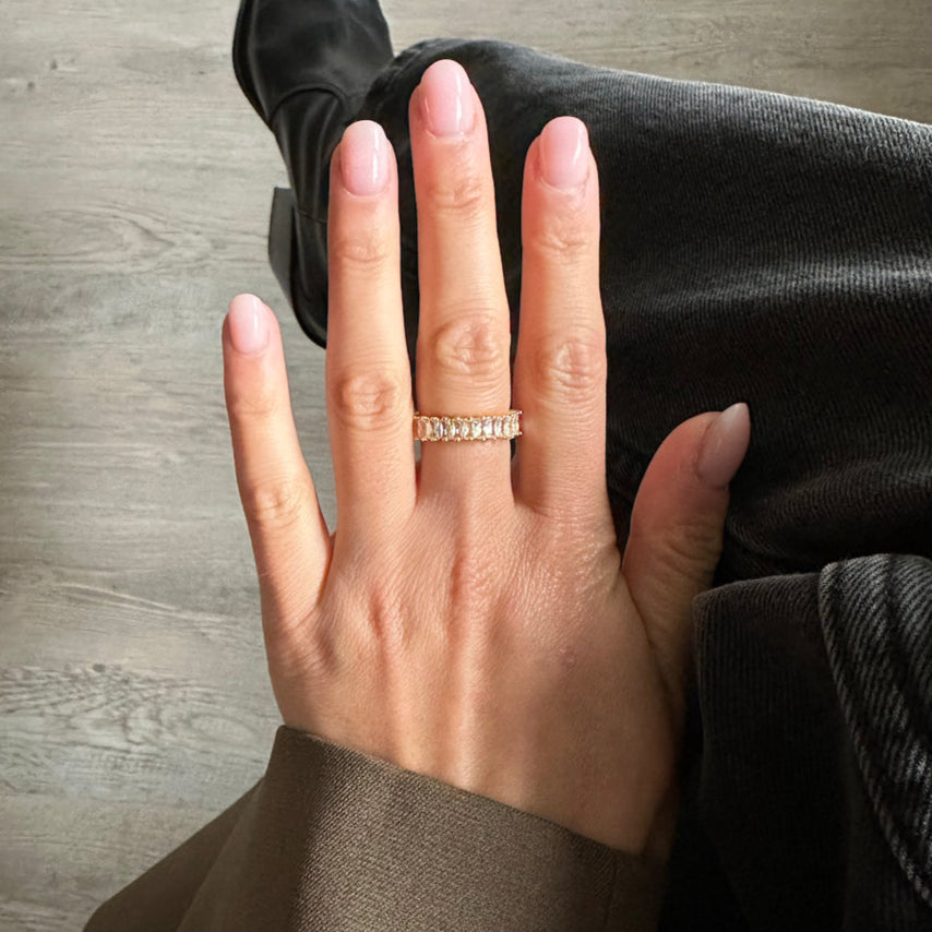 Goldener Baguette Ring an der Hand einer Frau, kombiniert mit lässigem Outfit in dunklen Tönen.