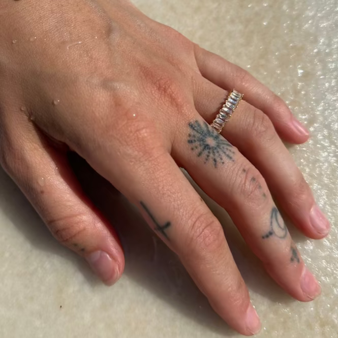 Goldener Baguette Ring an tätowierter Hand mit Wassertropfen auf hellem Steinuntergrund.