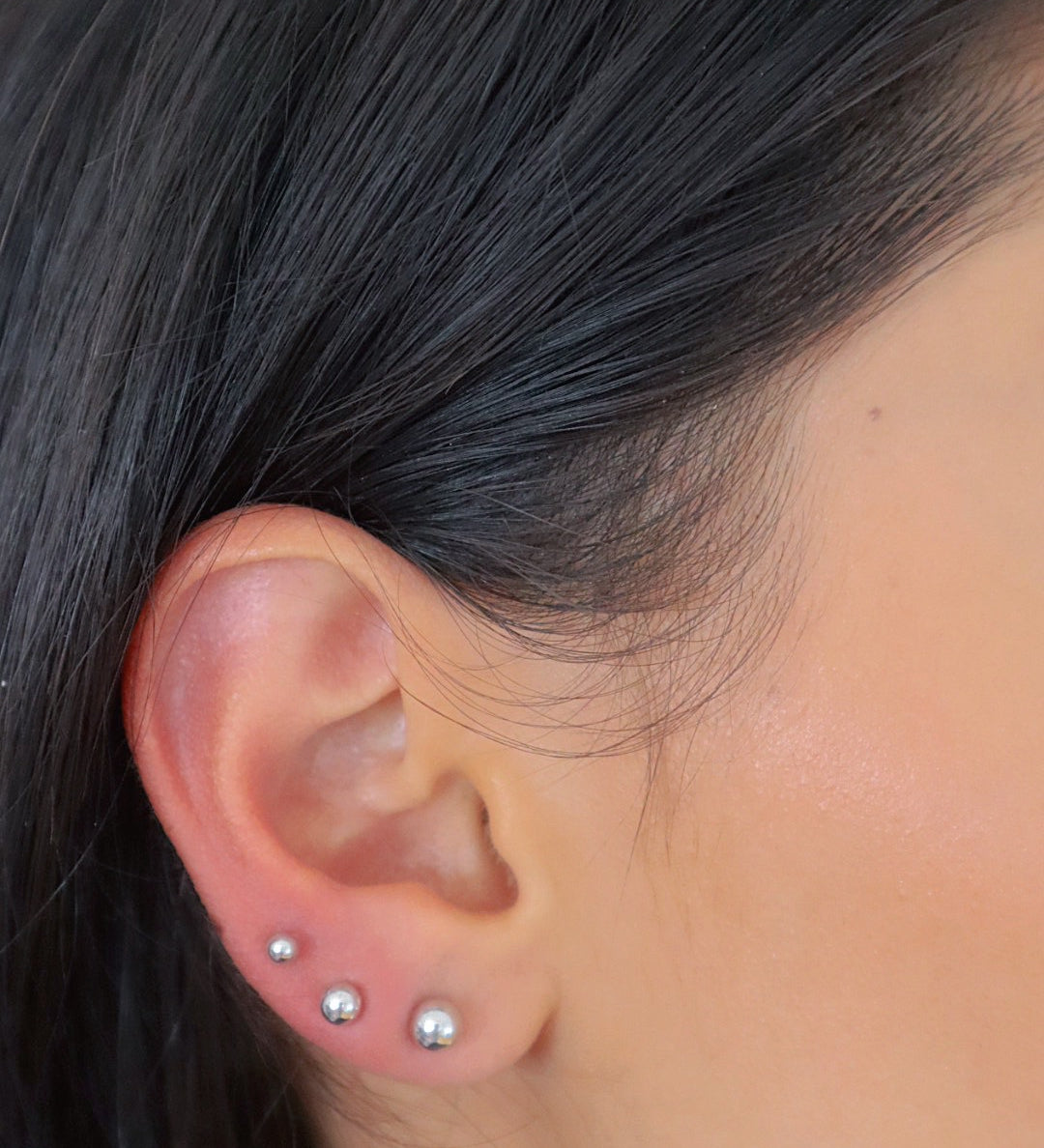 Silberne Balls L Stud Kugel-Ohrstecker aus 925 Sterling Silber in drei Größen am Ohr einer Frau getragen.