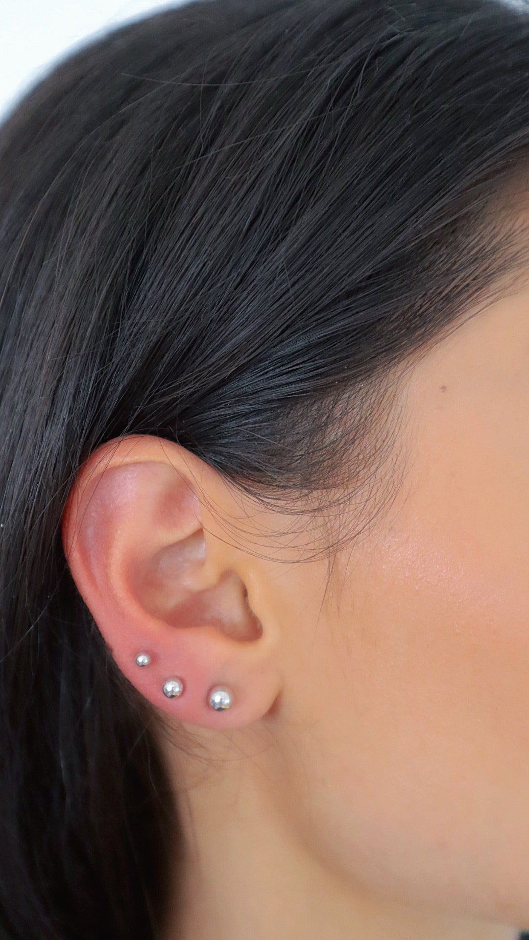 Silberne Balls L Stud Kugel-Ohrstecker aus 925 Sterling Silber in drei Größen am Ohr einer Frau getragen.