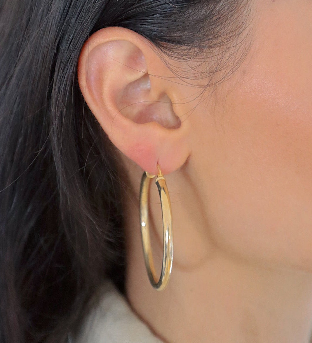 Frau trägt Bump L Creole in Gold am Ohr, elegante mittelgroße Reifenohrringe.