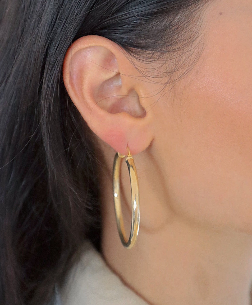 Frau trägt Bump L Creole in Gold am Ohr, elegante mittelgroße Reifenohrringe.