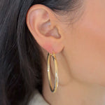 Frau trägt Bump L Creole in Gold am Ohr, elegante mittelgroße Reifenohrringe.