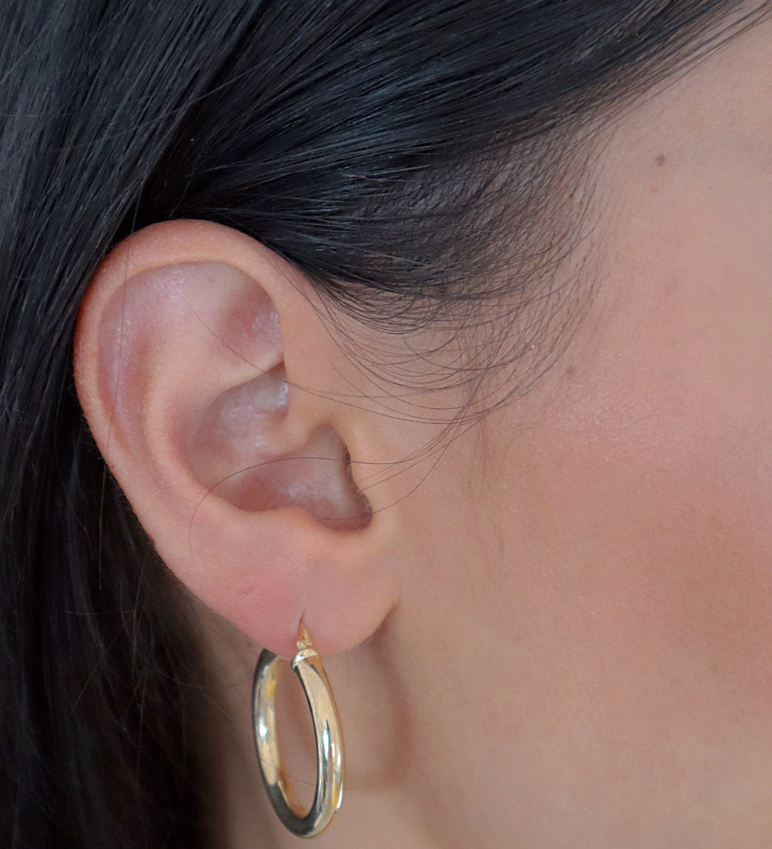 Bump M Creolen in Gold am Ohr einer Frau, mittelgroße elegante Hoops für Alltag und Abendlook.