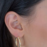 Bump M Creolen in Gold am Ohr einer Frau, mittelgroße elegante Hoops für Alltag und Abendlook.