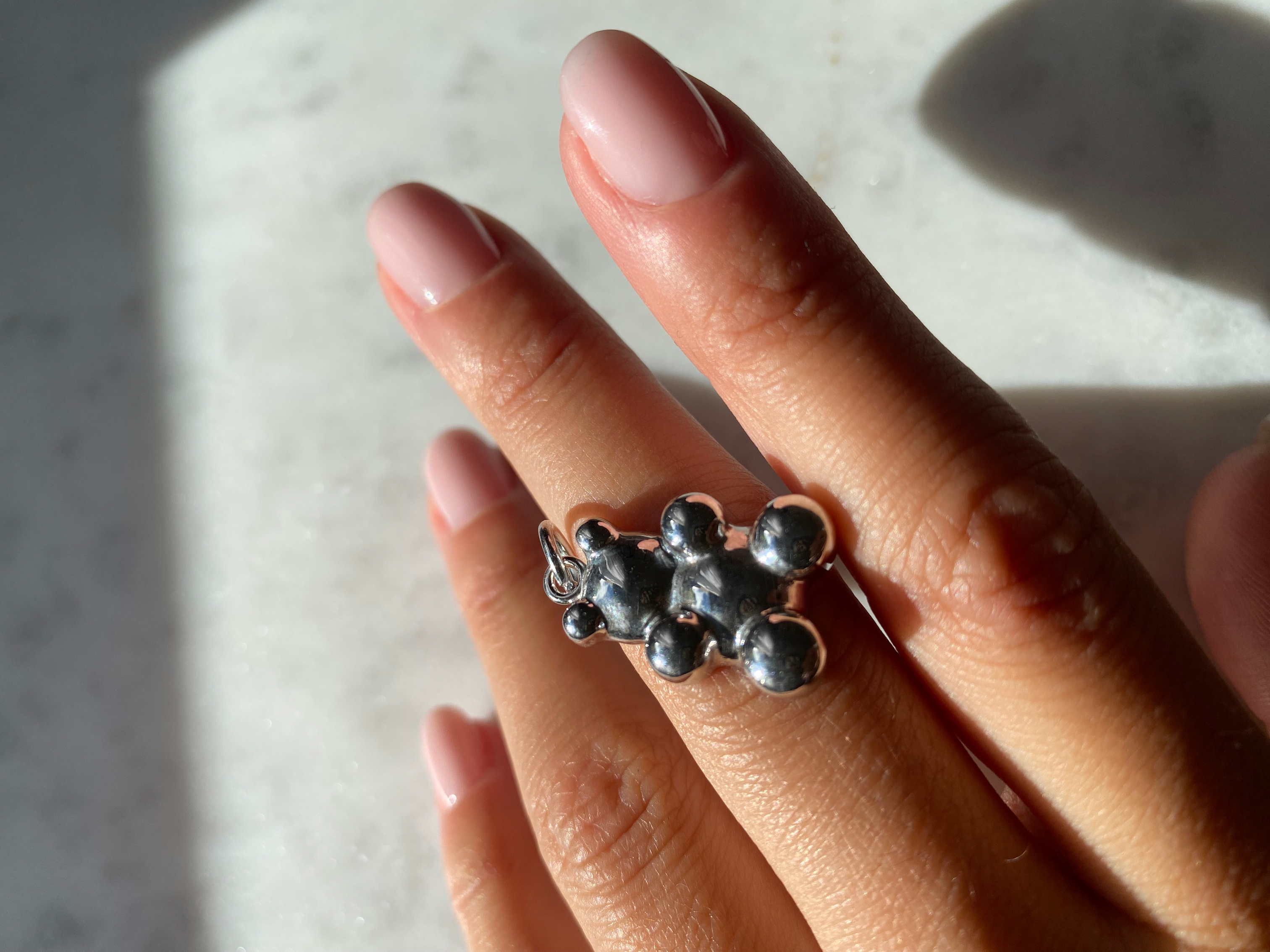 Clear Bear Anhänger Silber aus 925er Sterling Silber, liegend auf Fingern mit zart rosa Maniküre.