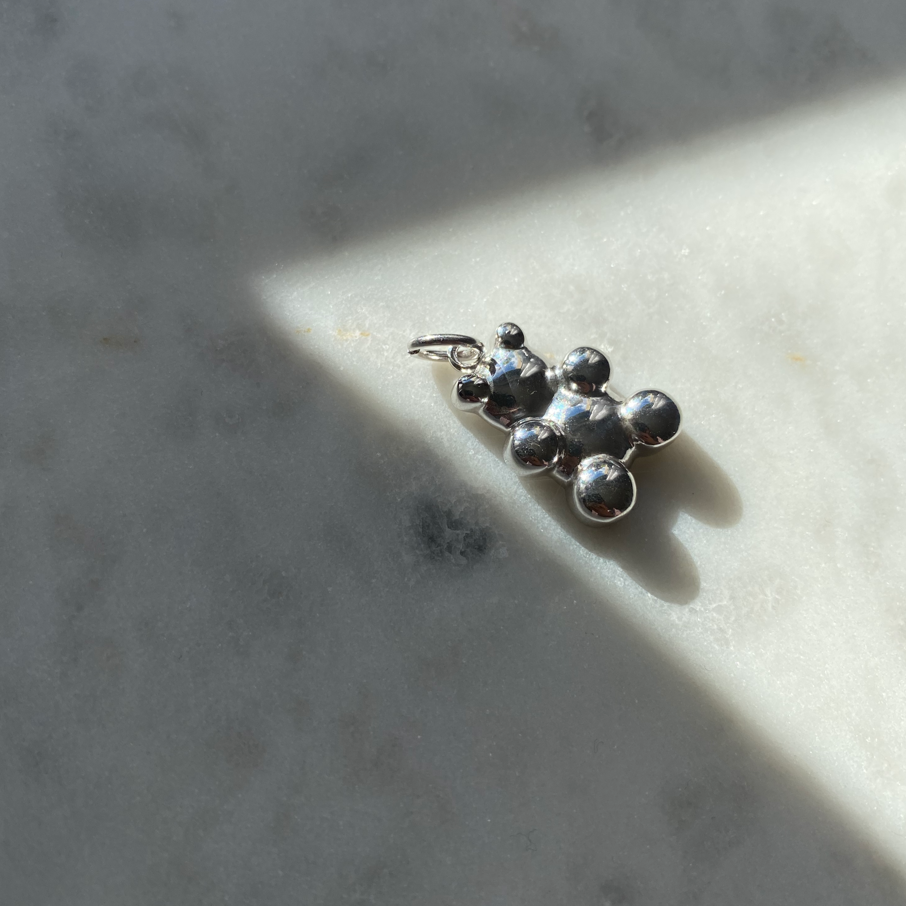 Silberner Clear Bear Anhänger aus 925er Sterling Silber, liegend im Sonnenlicht auf hellem Stein.