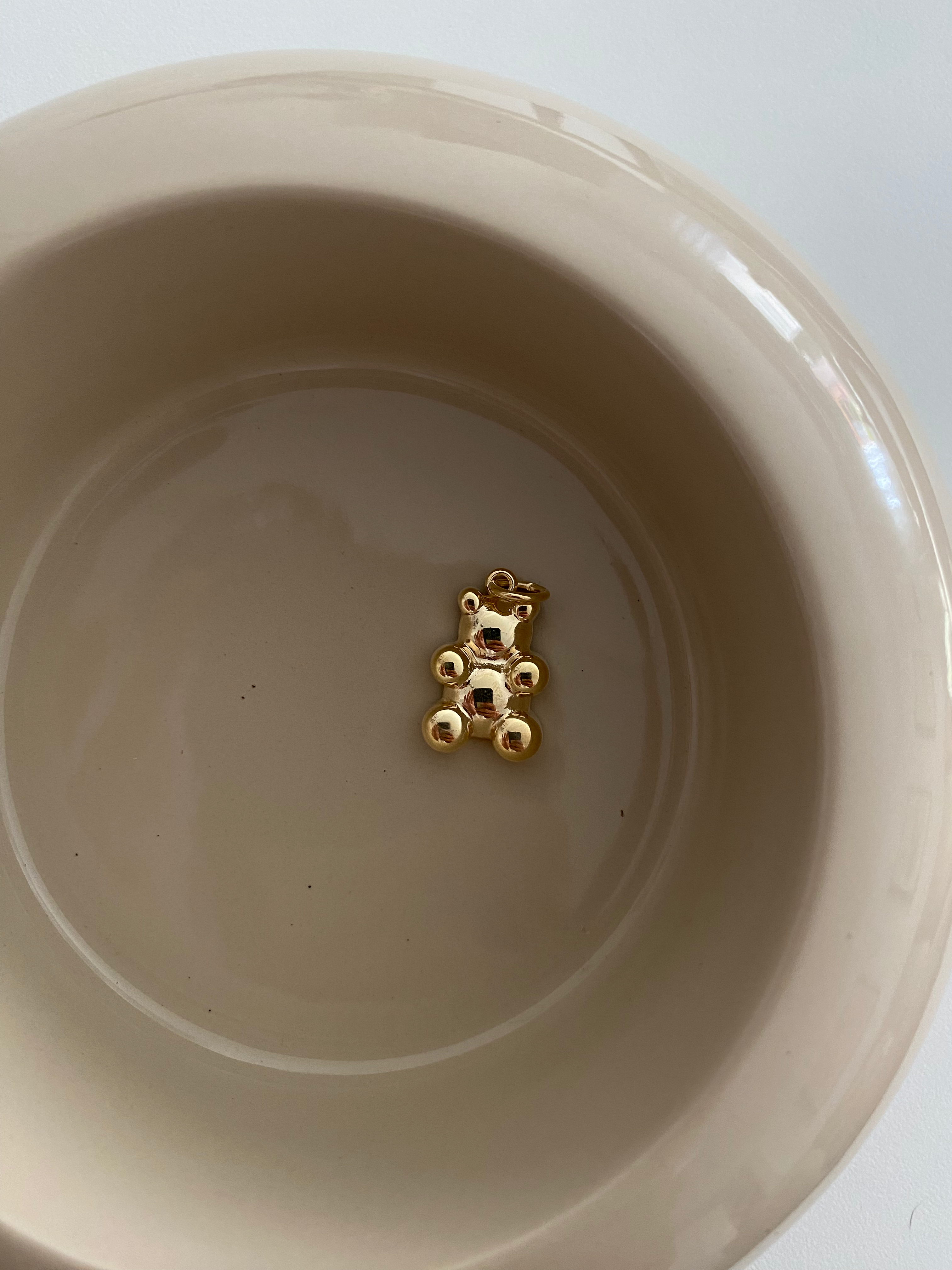 Clear Bear Anhänger Gold aus 925er Silber, liegend in beiger Keramikschale als minimalistisches Stillleben.