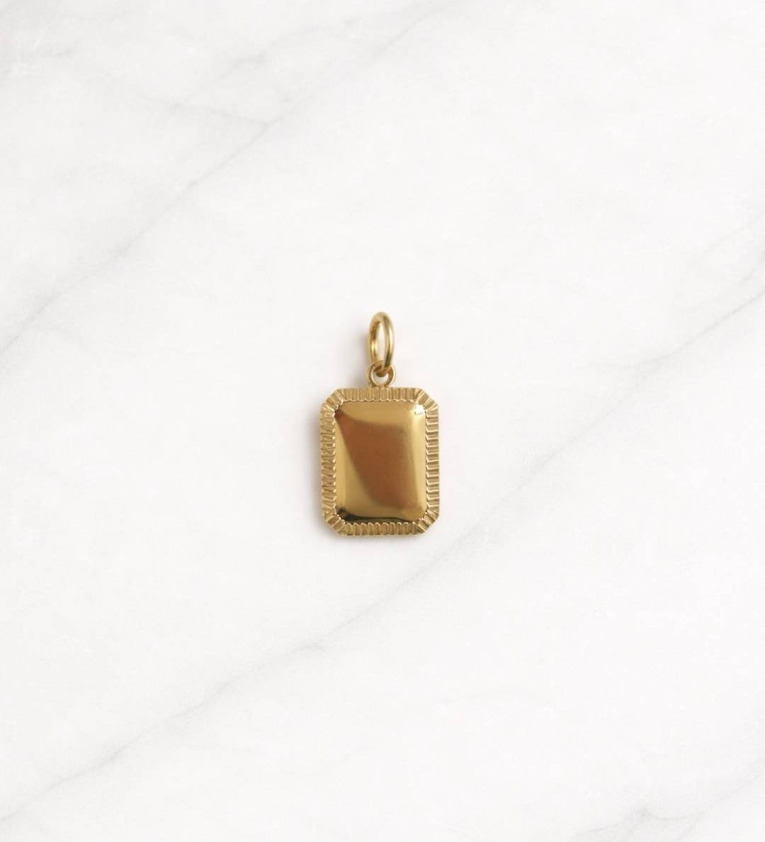 Copenhagen Charm in Gold als rechteckiger Anhänger auf hellem Marmorphintergrund.
