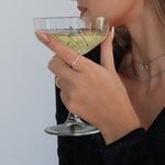 Hand mit Cross Ring in Silber und Cocktailglas, eleganter Dkeniz Damenring im Alltag getragen.