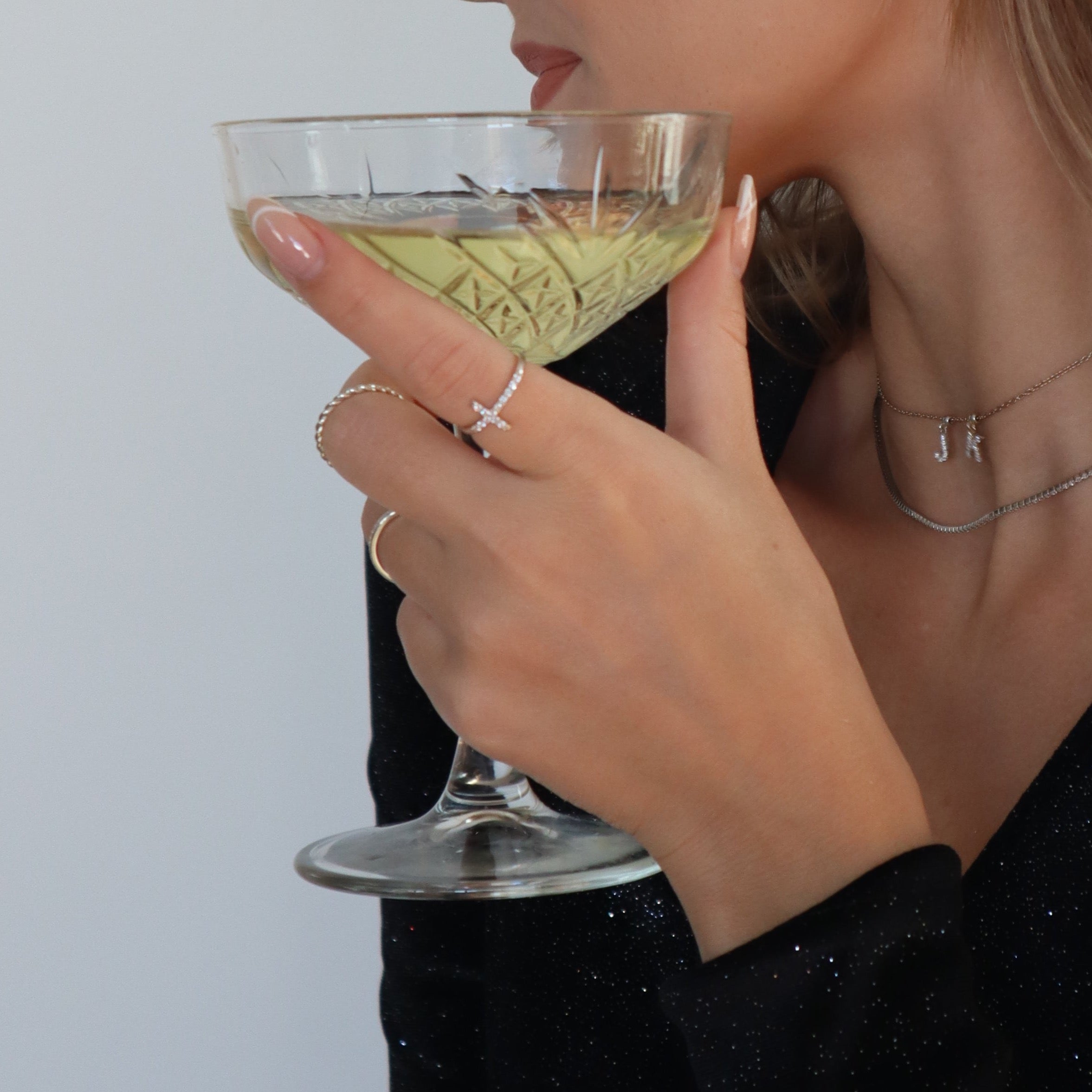 Hand mit Cross Ring in Silber und Cocktailglas, eleganter Dkeniz Damenring im Alltag getragen.