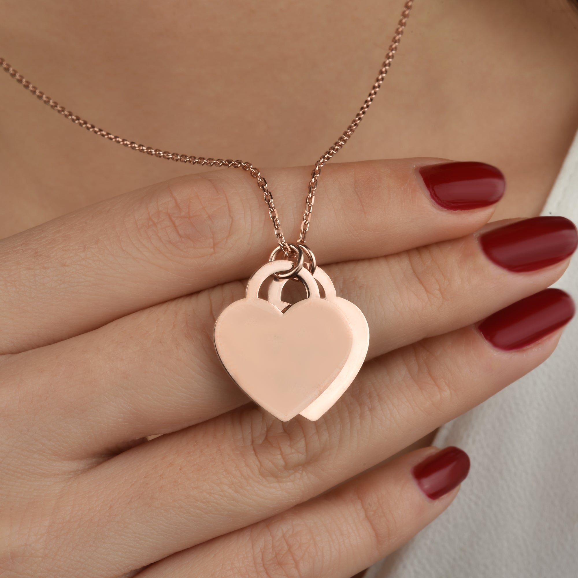 Double Heart Kette Rosé auf Hand mit rotem Nagellack, eleganter Look.