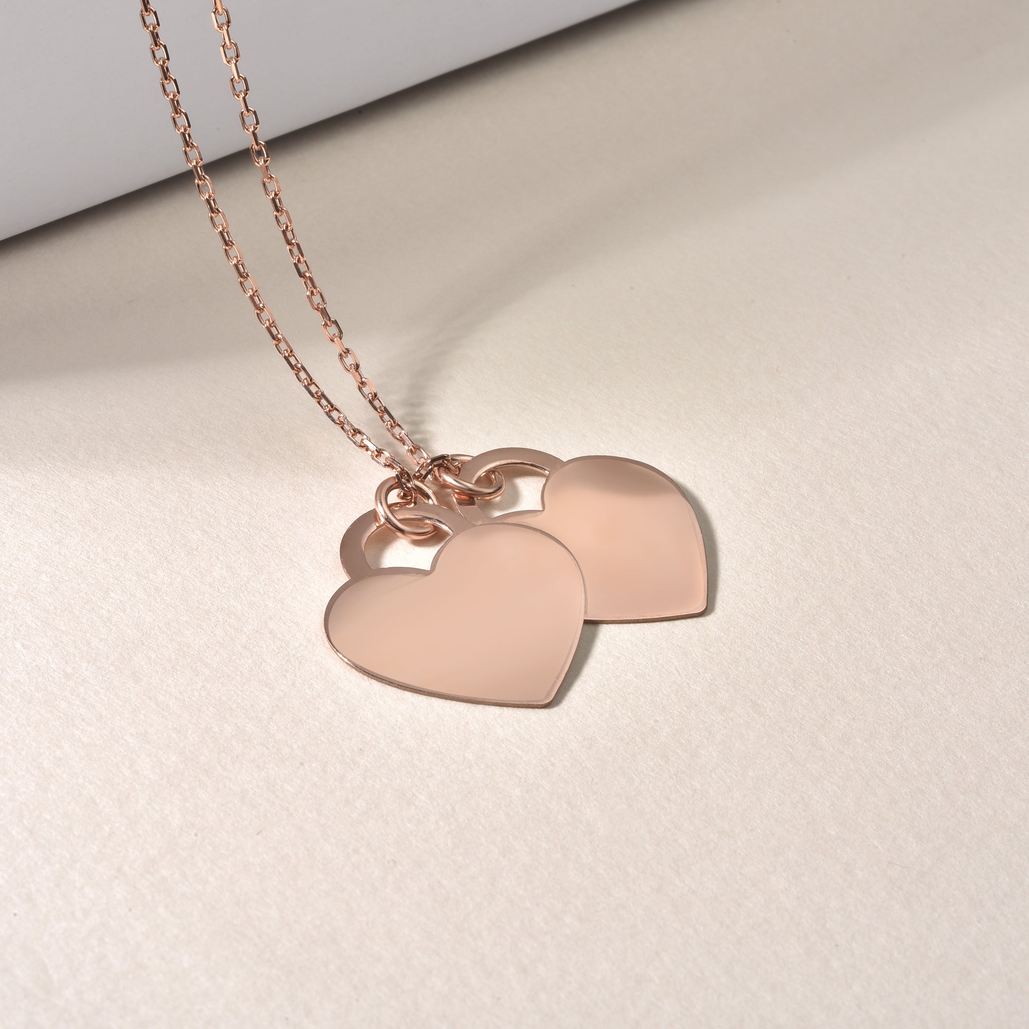 Double Heart Kette Rosé als Detailaufnahme auf hellem Untergrund, zwei Herzen.