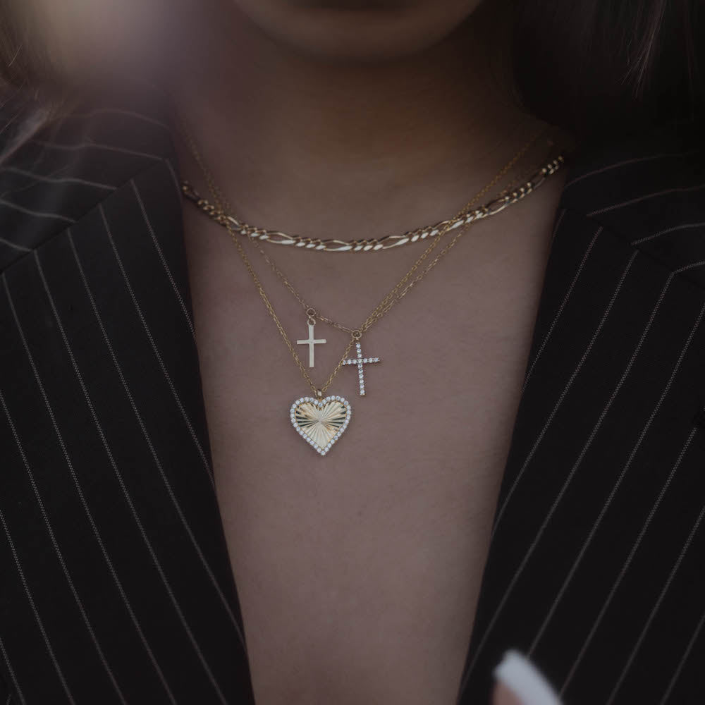 Layering mit Herz- und Double Kreuz Zirkonia Kette Gold auf dunklem Blazer.