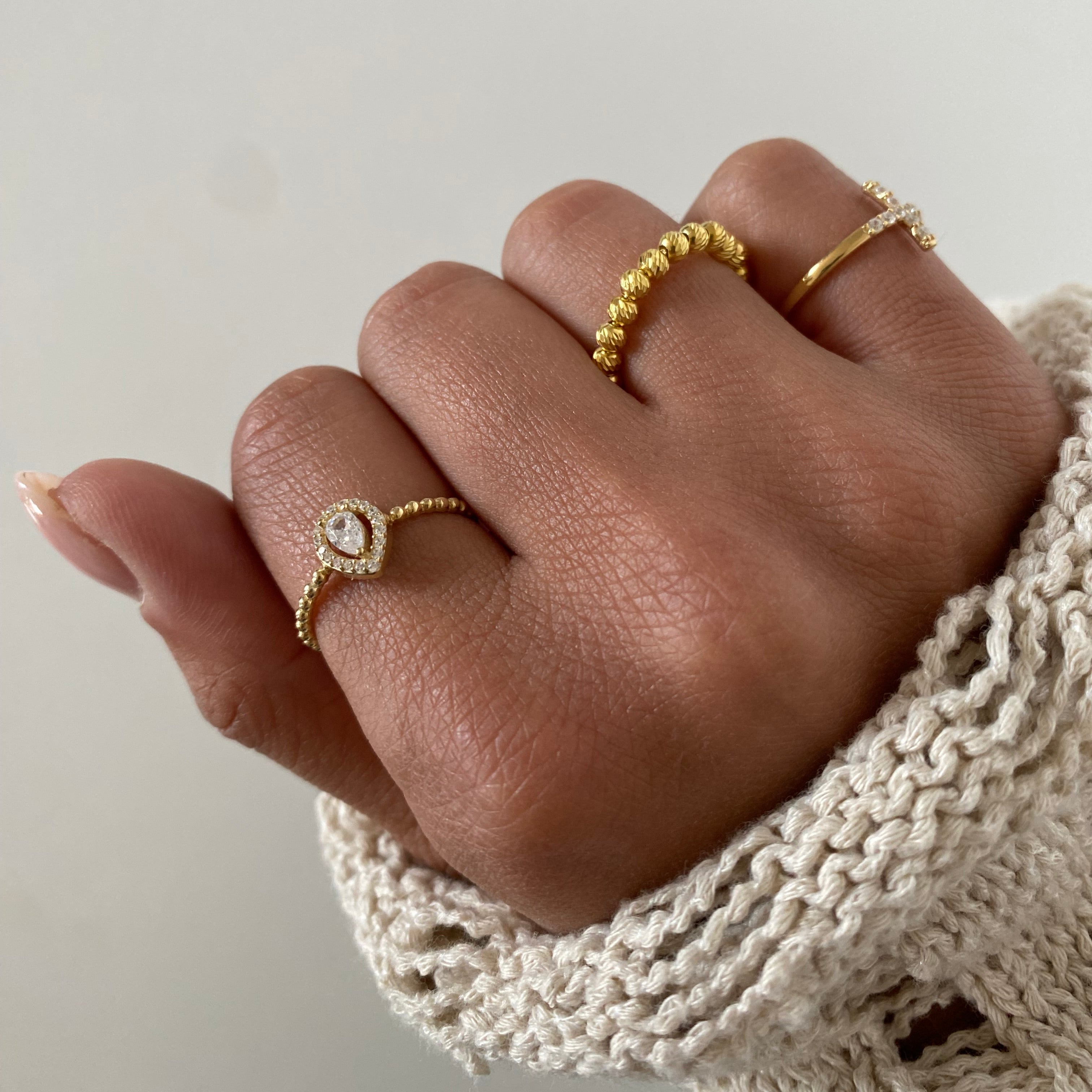 Drop Diamond Ring Gold mit Zirkonia an weiblicher Hand, kombiniert mit weiteren Goldringen.
