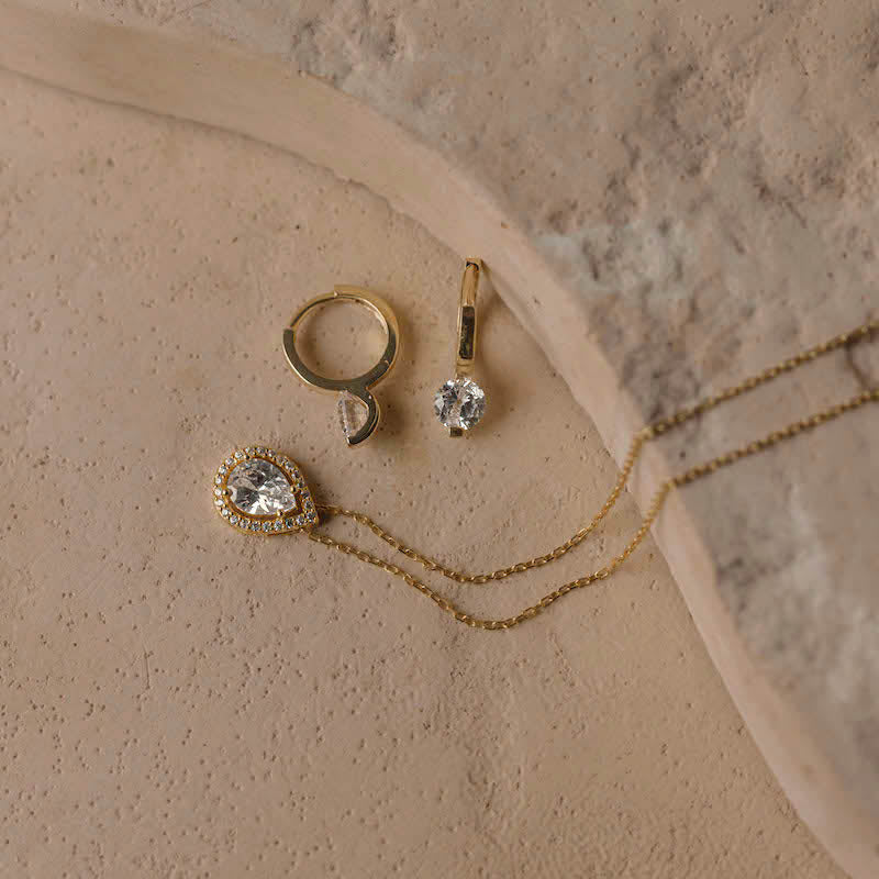 Flatlay: Drops Halskette Gold mit Zirkonia Tropfen-Anhänger neben passenden goldenen Ohrringen.