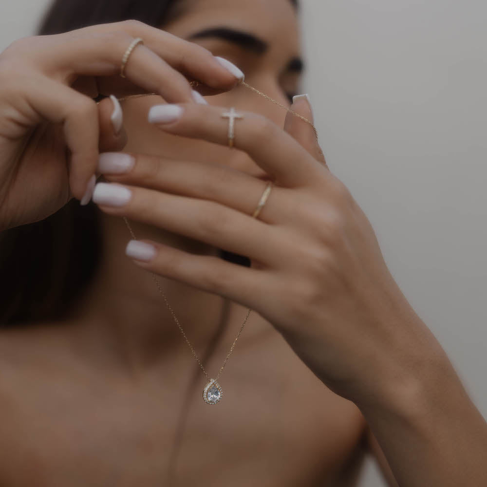 Model hält die goldene Drops Halskette mit Zirkonia Tropfen-Anhänger in den Händen, Detailaufnahme.