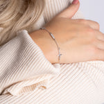 Filigrane Silber-Arm­kette mit Kreuz und Zirkonia am Handgelenk, eleganter Look in Beige.