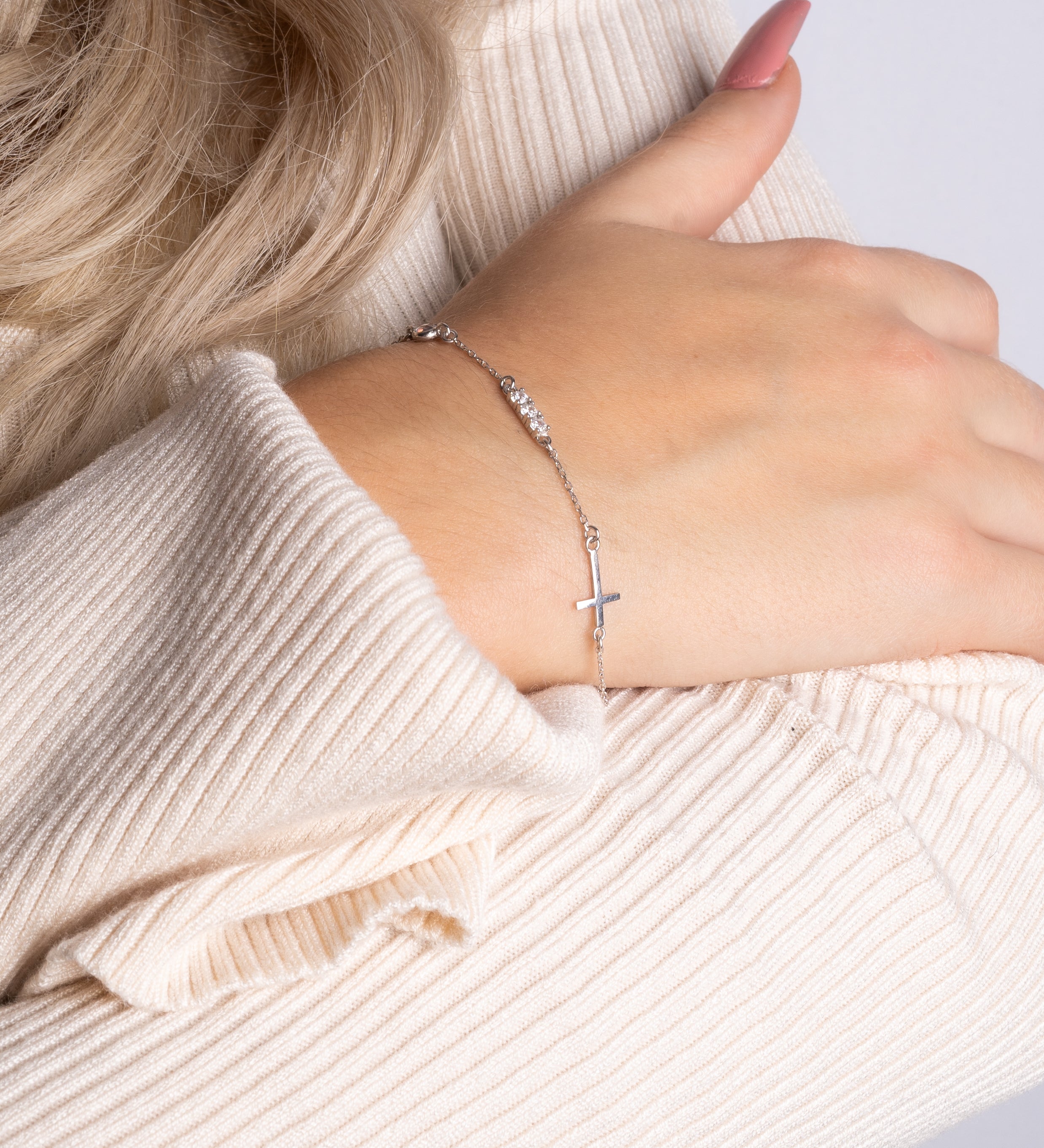 Filigrane Silber-Arm­kette mit Kreuz und Zirkonia am Handgelenk, eleganter Look in Beige.