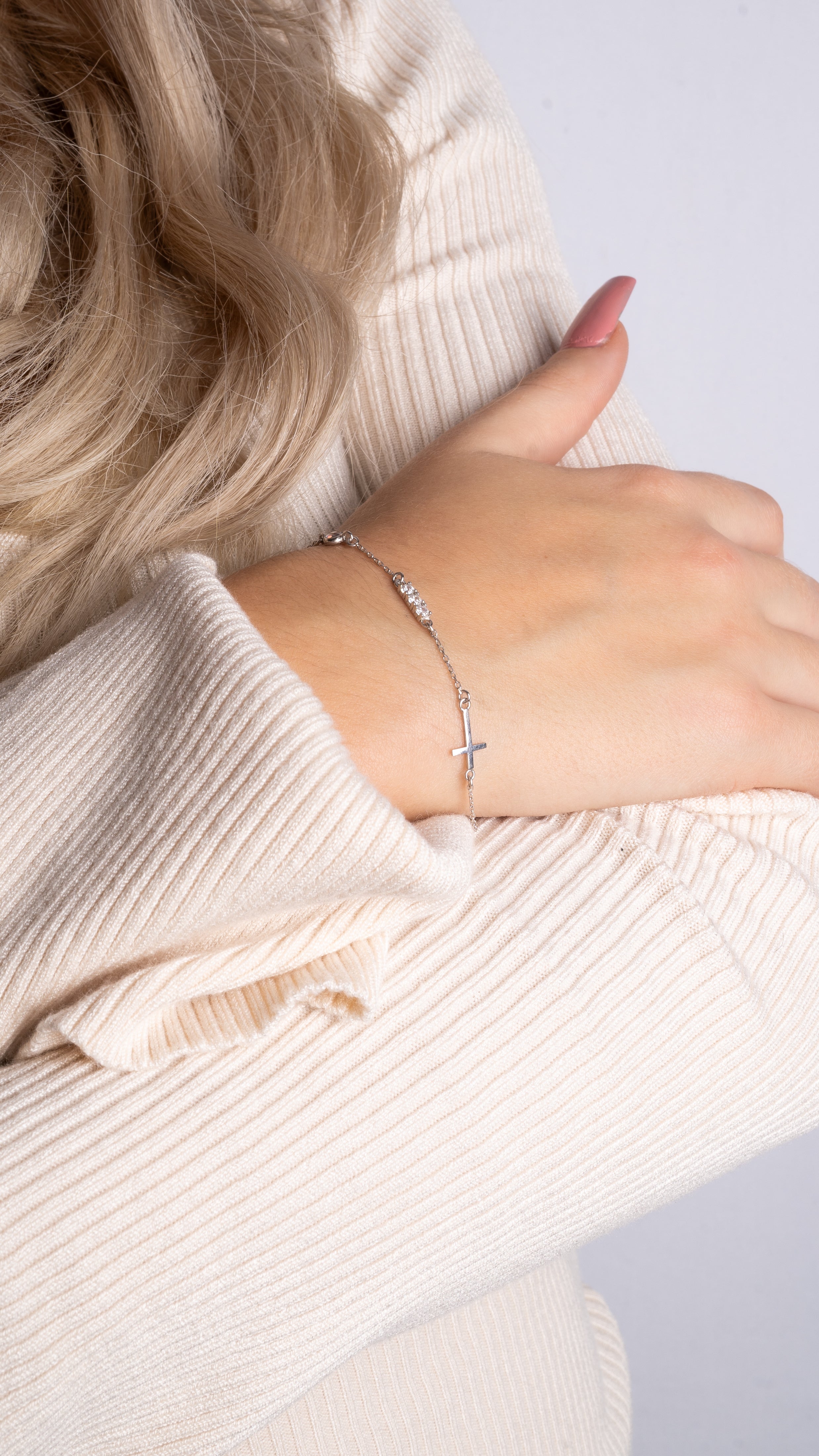 Filigrane Silber-Arm­kette mit Kreuz und Zirkonia am Handgelenk, eleganter Look in Beige.