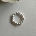 Perl Ring mit weißen Perlen und goldener Kugel auf heller Tischoberfläche.