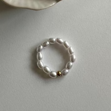 Perl Ring mit weißen Perlen und goldener Kugel auf heller Tischoberfläche.