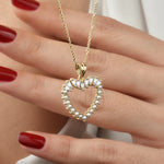 Close-up: Herz-Anhänger mit Perlen und Baguette-Zirkonia an goldener Kette auf der Hand.