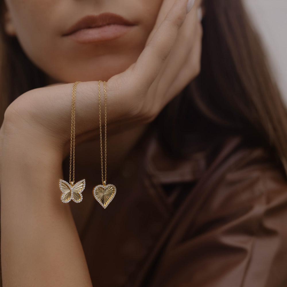 Herz Halskette Gold mit Zirkonia neben Butterfly-Anhänger – Shiny Collection Schmuck am Handgelenk.