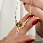 Hand präsentiert goldene Infinity Angel Wings Halskette mit funkelnden Zirkonia-Steinen.