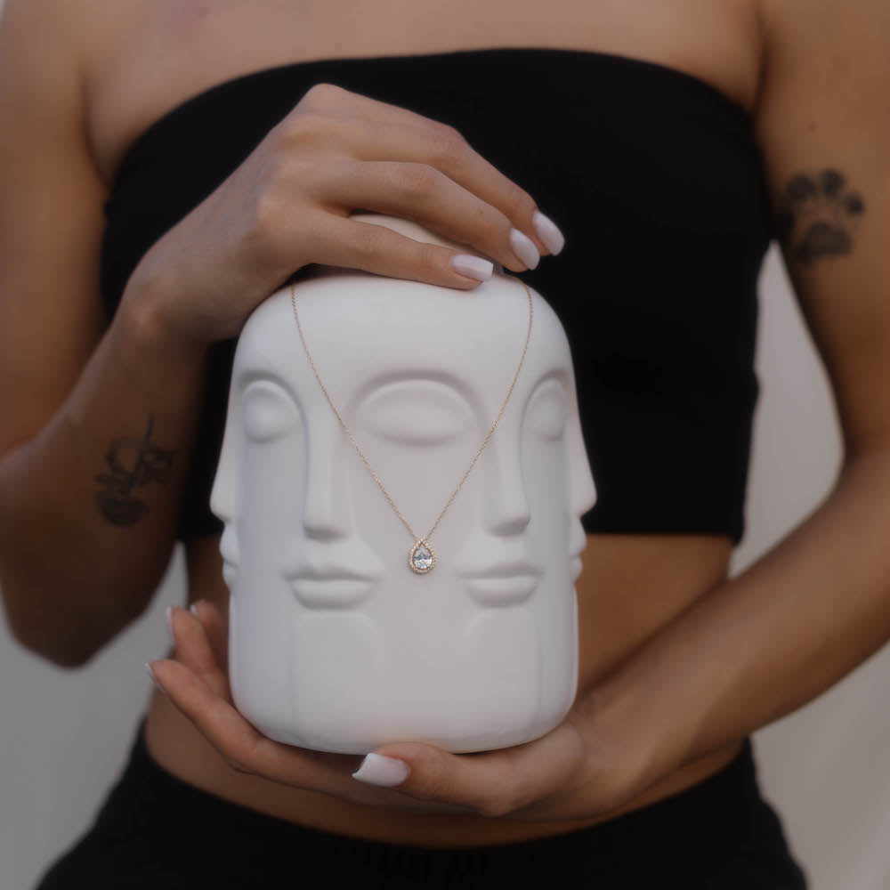 Goldene Kette mit Tropfenanhänger aus Edelstahl, präsentiert auf weißer Gesichtsstatue, minimalistischer Damenschmuck für besondere Anlässe.