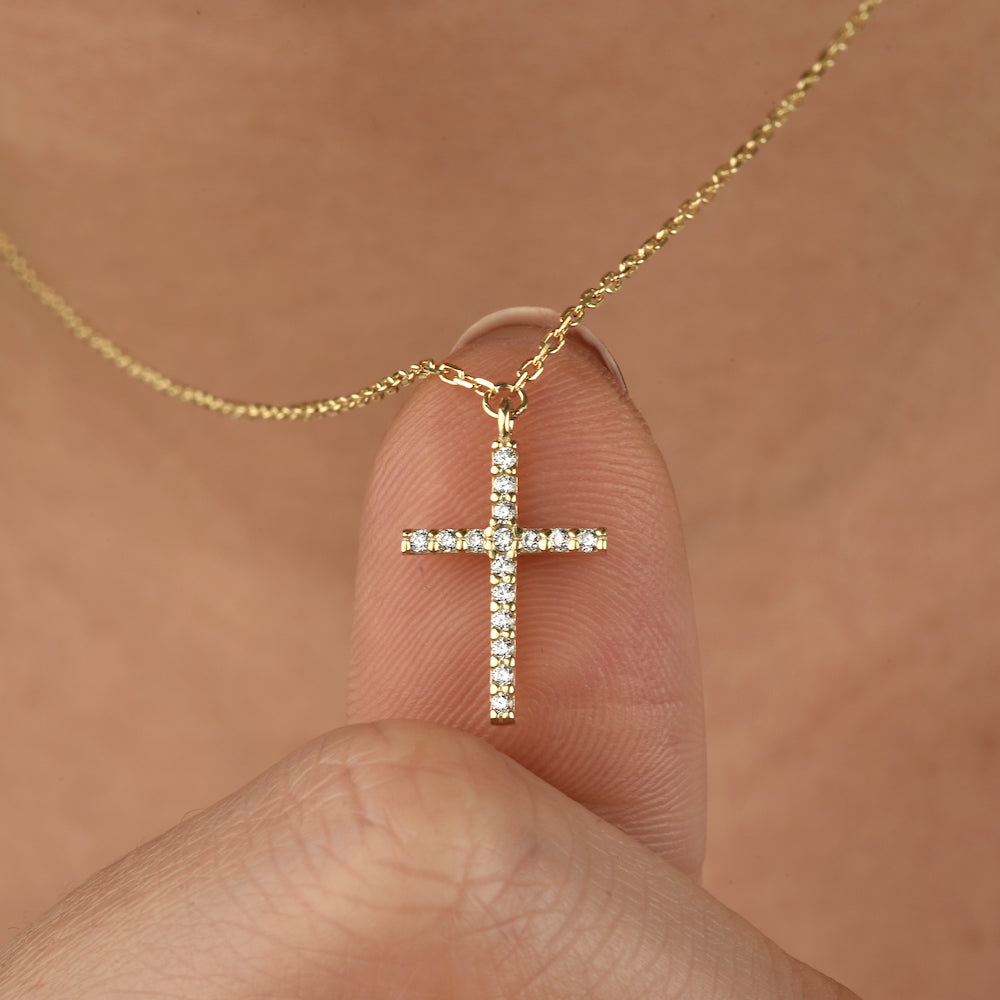 Detailaufnahme: Kreuz Anhänger mit weißen Zirkonia an goldener Kette, gehalten zwischen den Fingern.