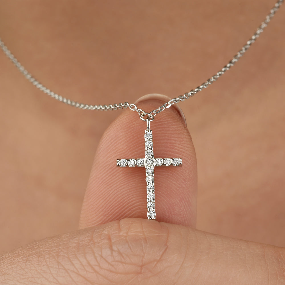 Nahaufnahme einer silbernen Kreuz Zirkonia Kette, gehalten zwischen den Fingern.