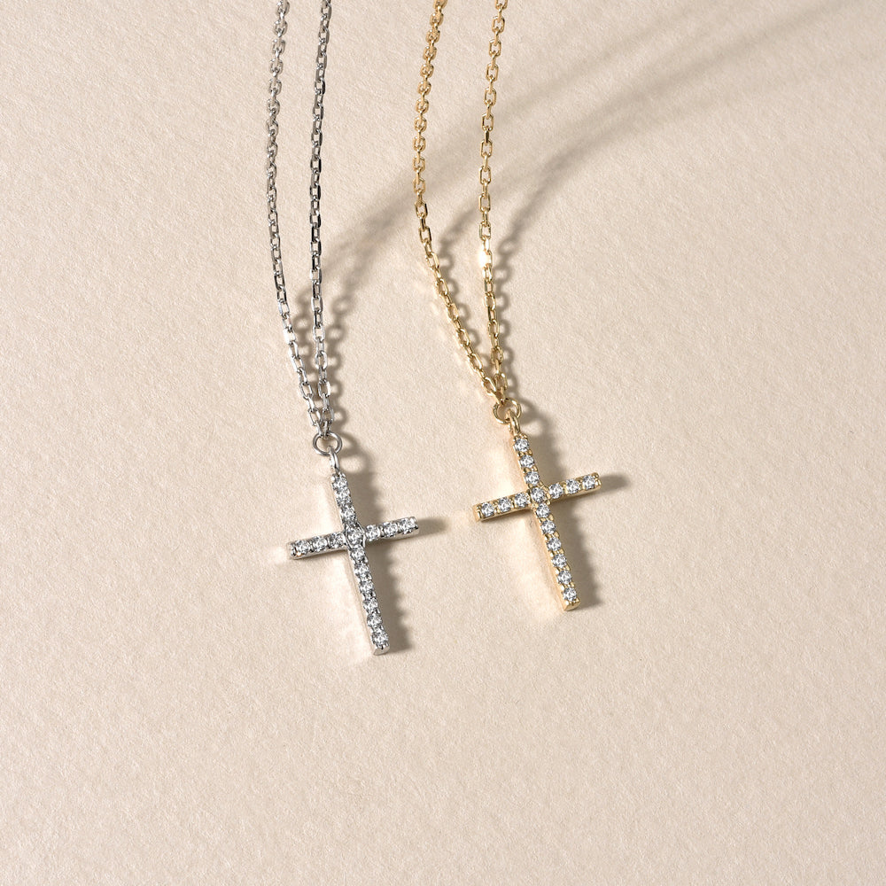 Silberne und goldene Kreuz Zirkonia Ketten flach auf beigem Untergrund liegend.