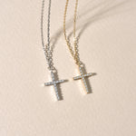 Silberne und goldene Kreuz Zirkonia Ketten flach auf beigem Untergrund liegend.