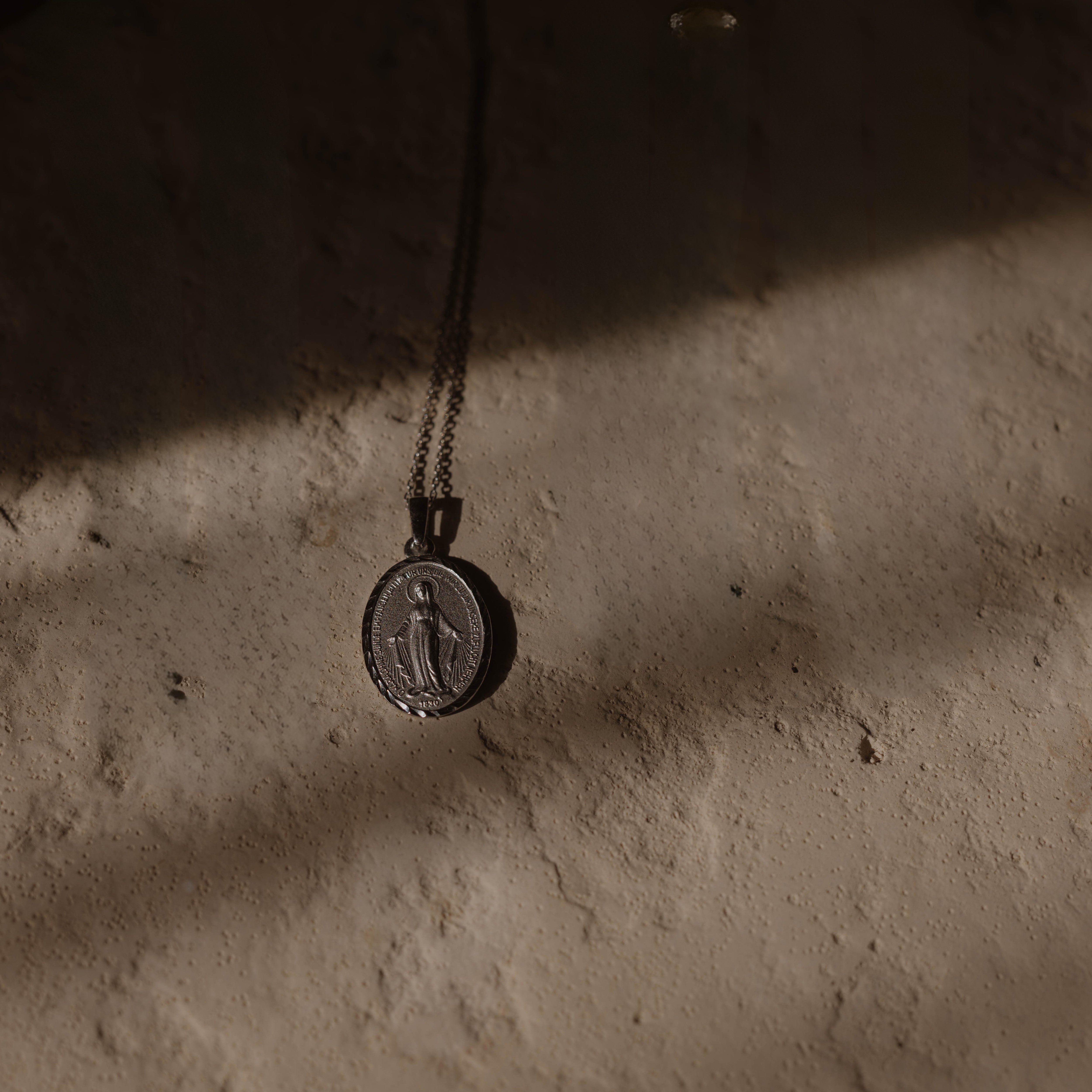 Silberne Madonna Kette als Moodbild, Anhänger hängt an feiner Kette vor Strukturuntergrund.