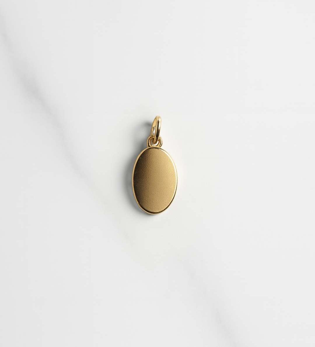 Vergoldeter ovaler Mailand Charm auf hellem Marmorfond, ideal für Personalisierung und Mix and Match Ketten