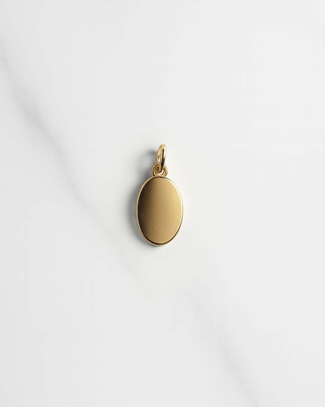 Vergoldeter ovaler Mailand Charm auf hellem Marmorfond, ideal für Personalisierung und Mix and Match Ketten