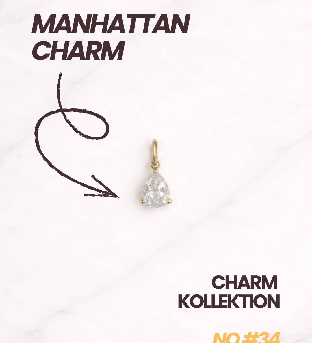 Manhattan CHARM Gold Anhänger mit Schriftzug und Pfeil auf den Charm und hellem Hintergrund.