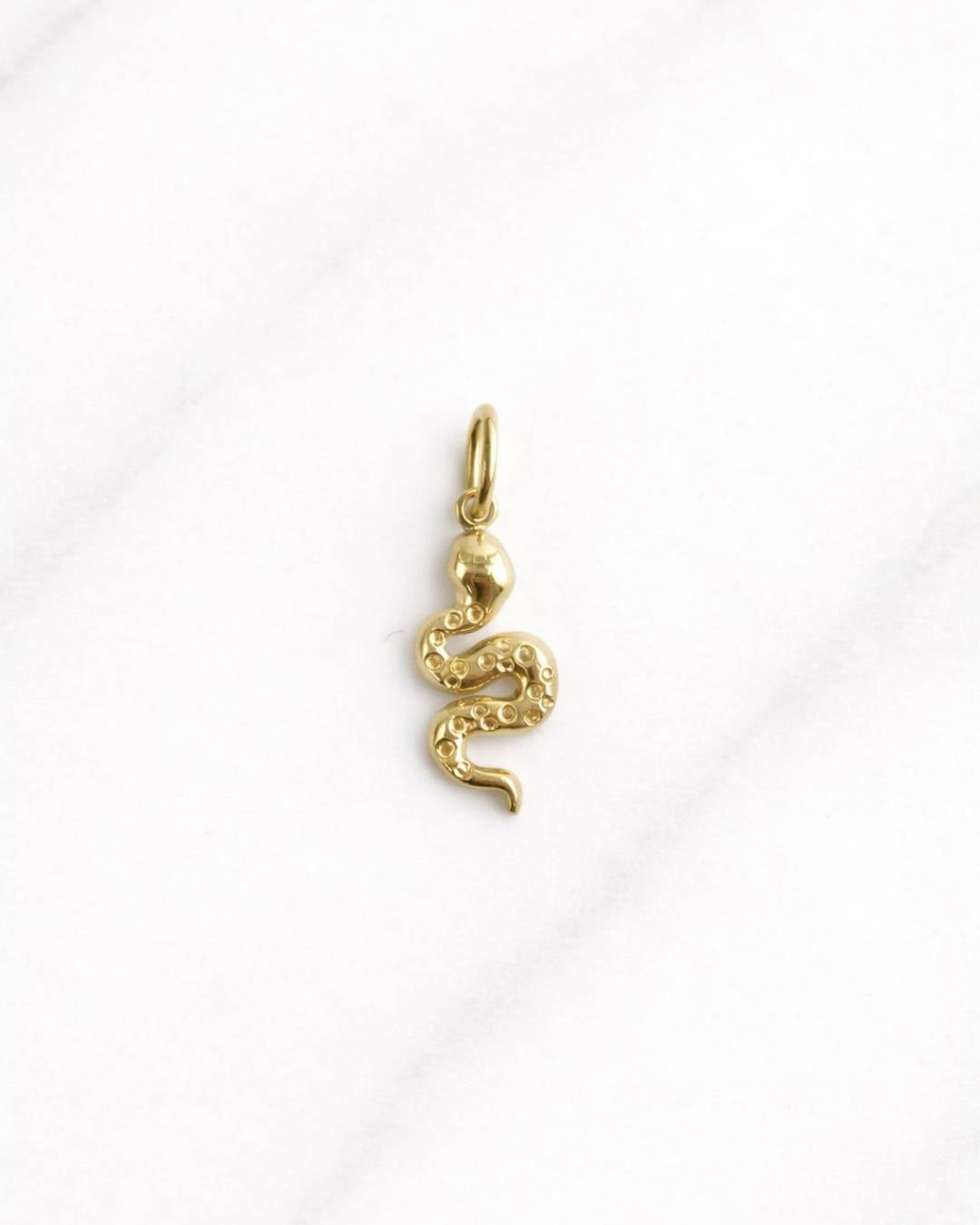 Goldener Marrakesh CHARM als filigraner Schlangenanhänger auf hellem Marmorhintergrund, Schmuck für Damen.