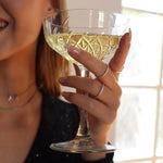 Hand mit Sektglas, getragen wird der Memori Zirkonia Ring in Silber als filigraner Stapelring.