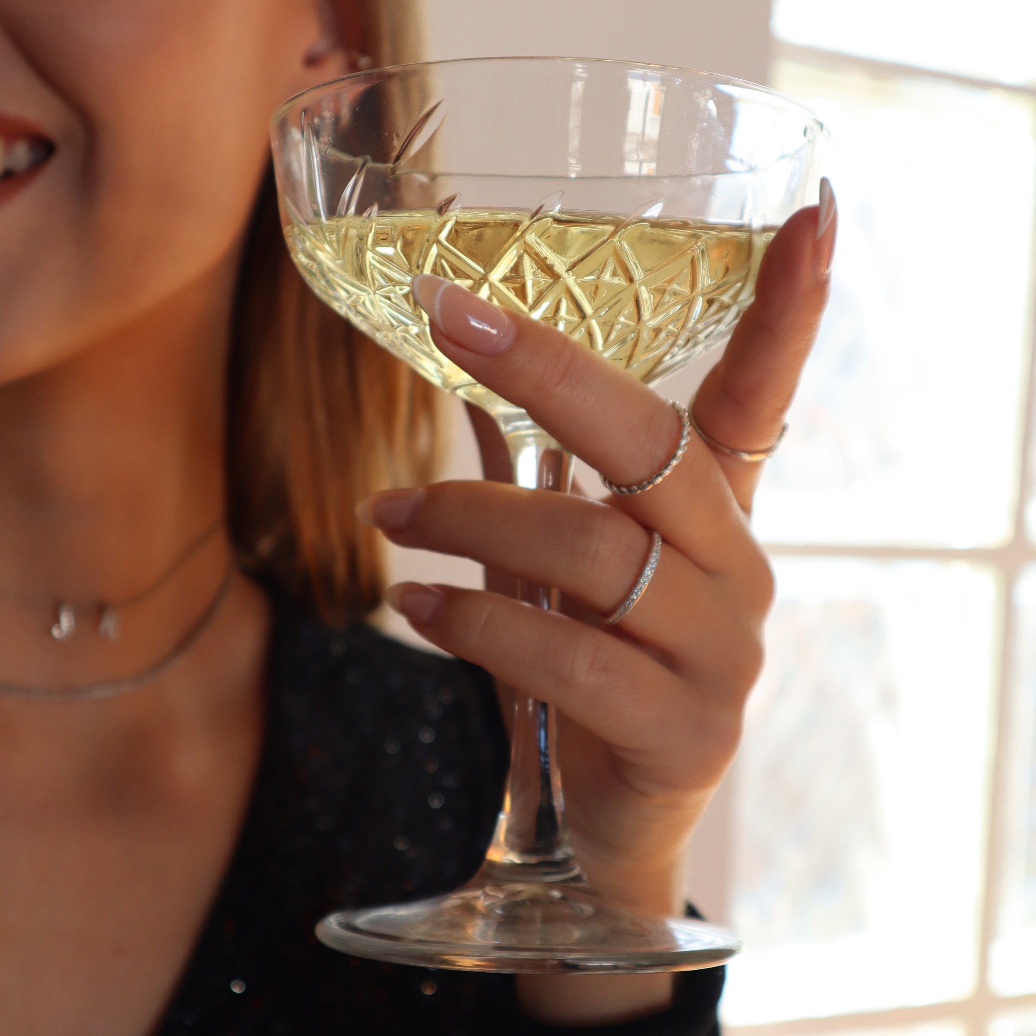 Hand mit Sektglas, getragen wird der Memori Zirkonia Ring in Silber als filigraner Stapelring.