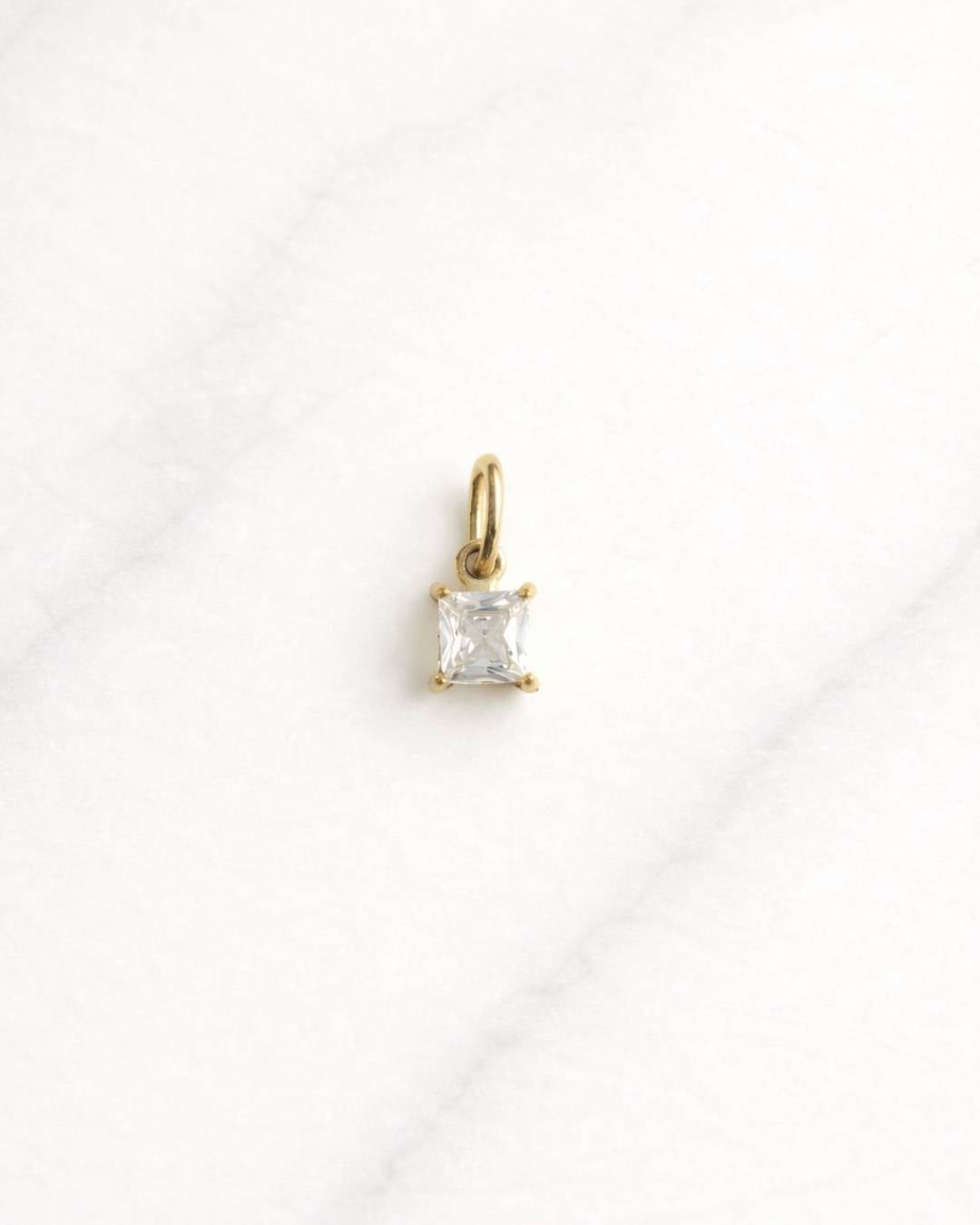 Milan CHARM Gold mit quadratischem Zirkonia auf hellem Marmor-Hintergrund.