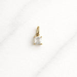 Milan CHARM Gold mit quadratischem Zirkonia auf hellem Marmor-Hintergrund.