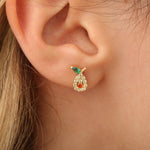 Avocado-Ohrstecker am Ohr, weiße und orangene Steine und grünes Blatt, filigranes Design.